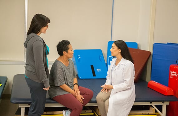 Two women are sitting at a table while another woman standing beside them speaking to each other
