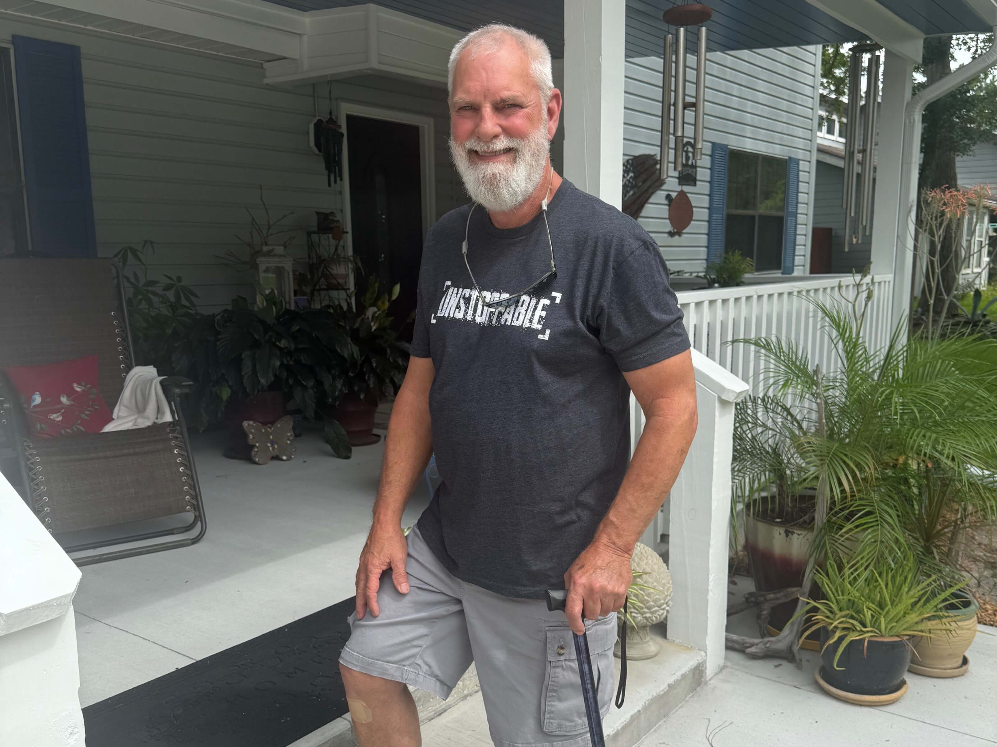 Danny stands by the stairs of his front porch, using his cane for support, after returning home from UF Health Rehabilitation.