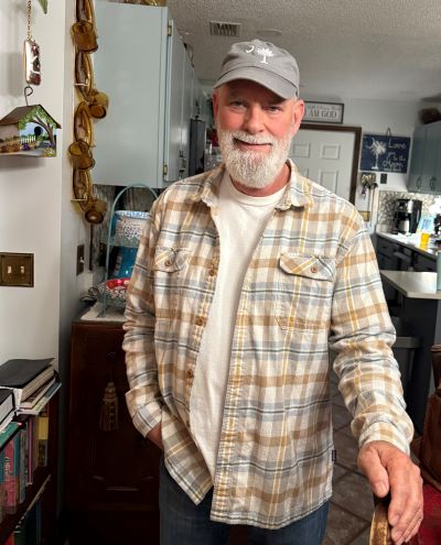 Danny stands in his house smiling at the camera after recovering from stroke.