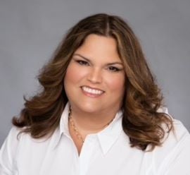 Allison Hirtzel smiles at the camera wearing a white collared shirt.