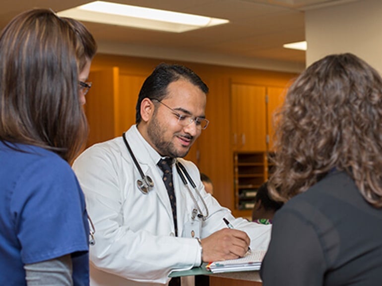 Male doctor and two female nurses meet by the nurses station to review a patient's chart.