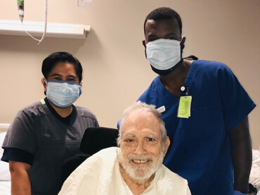 James sitting up in his hospital bed and two male therapists standing behind him.